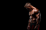 Very muscular gym man posing shirtless looking down isolated on a black background. Copy space design