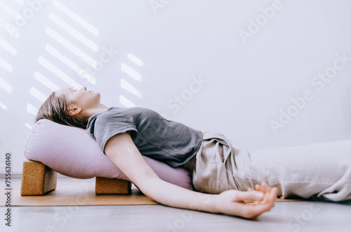 Woman in casual clothing doing yin/restorative yoga with bolster supported by blocks © Cristina