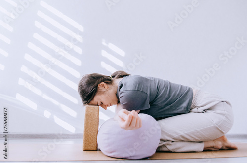 Woman in casual clothing doing yin yoga crossed arm stretch with bolster and cork block