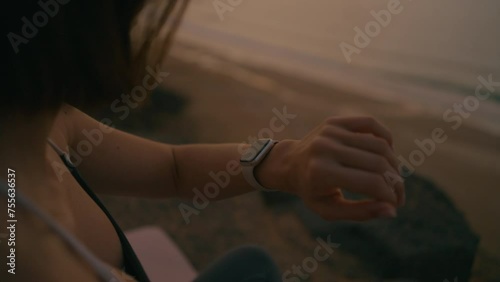 Close up of Woman doing yoga and checking smart watch on the edge of the cliff by the ocean at sunset, Fuerteventura, Spain