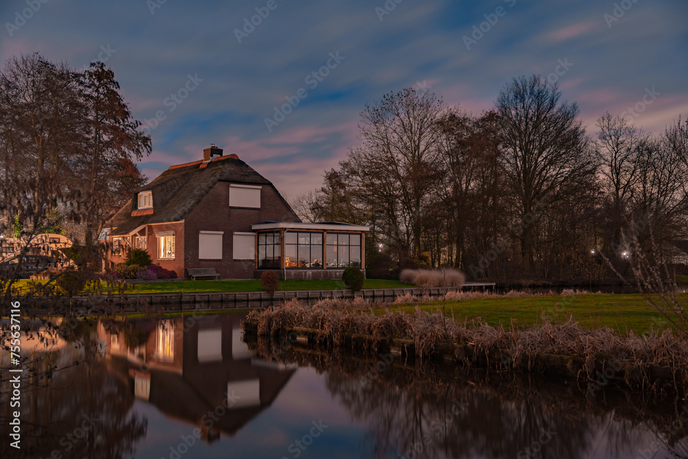 Fototapeta premium Night landscape with starry sky in the Dutch village of Streefkerk. Houses with bright light reflecting in the shine of the water in the autumn season