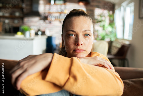 Pensive woman sitting on couch at home with a contemplative expression