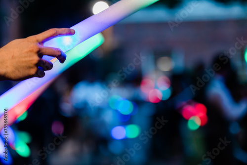 An abstract image of people holding light up colorful foam wands as the bride and groom leave the ceremony at a wedding at night with bokeh