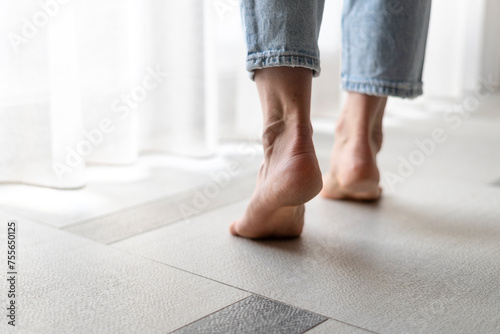 Female feet standing barefoot on tiled warm floor in living room