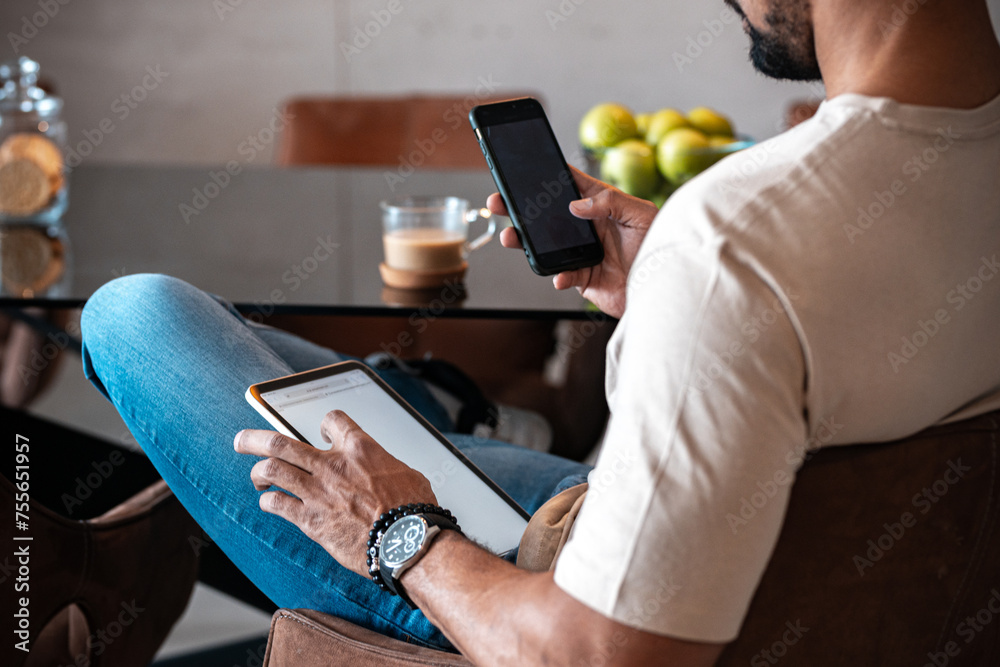 Fototapeta premium Close up of a young black man using tablet in living room and reading news and drinking coffee