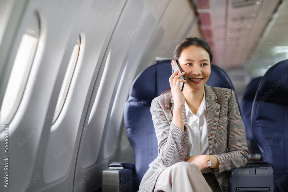 Young asian woman sitting on seat in airplane and talking by smartphone. Young woman traveller talking on cell phone Young asian woman sitting on seat in airplane and talking by smartphone. Young woman traveller talking on cell phone