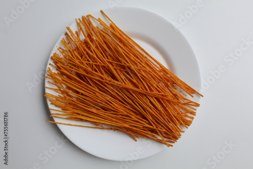 Mie lidi pedas, traditional snack from Indonesia. Noodle-like texture, fried and coated with chili powder. On white plate, isolated on white background, flat lay or top view photo