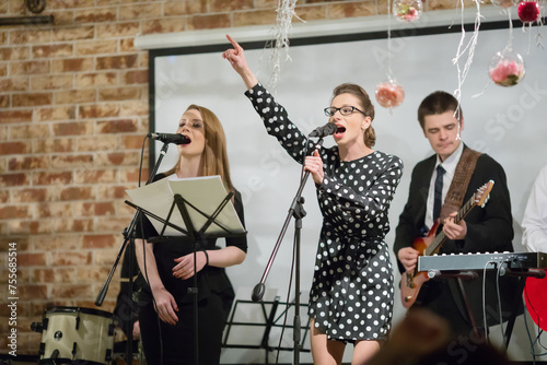 Two women sing and men play music ob stage during perfrom photo