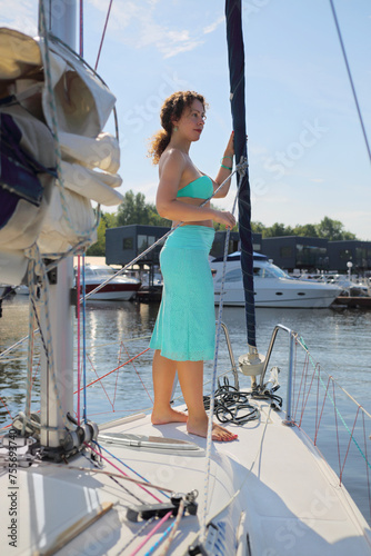 Woman in skirt stands on yacht during sailing on river at sunny summer day