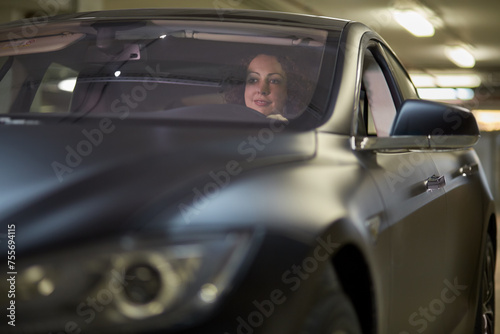 Smiling woman sits in modern car at underground parking
