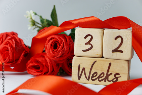 32 week gestational age milestone written on a wooden cube with red roses and ribbons, and a white background