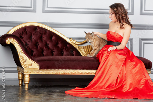 Woman in red dress sits on couch and plays with lynx cub