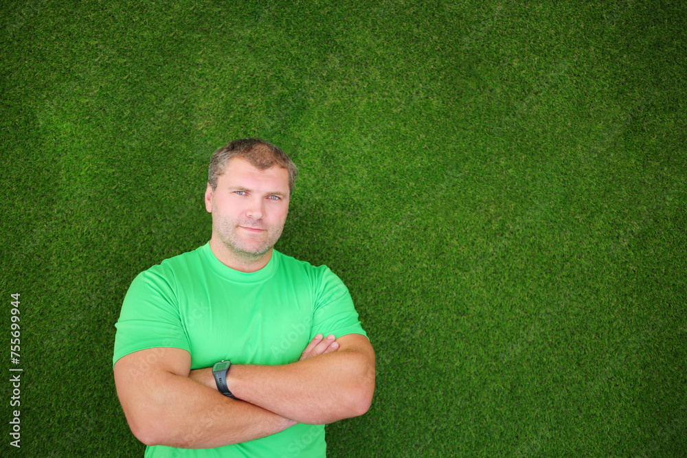 Young muscular man in t-shirt stands near green wall with crossed arms Young muscular man in t-shirt stands near green wall with crossed arms