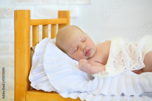 Cute baby sleeps in wooden small bed with white plaid in studio