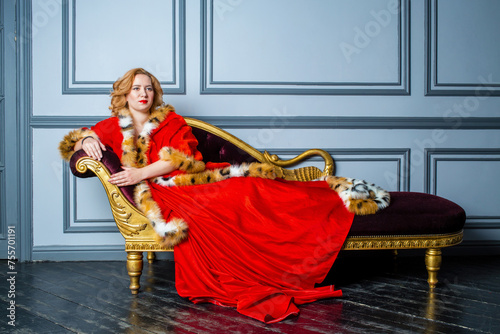 Blonde woman in red dress and cloak lies on couch in room photo