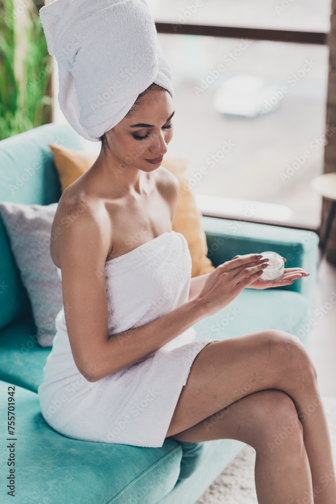 Vertical photo of pretty american female person bare shoulders sit sofa hold hydrating balm jar daylight flat indoors