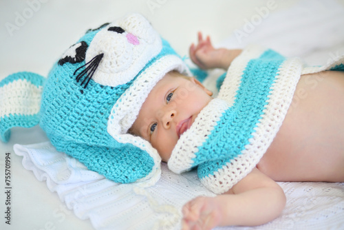 Cute little baby in blue rabbit hat lies on blanket in white studio photo