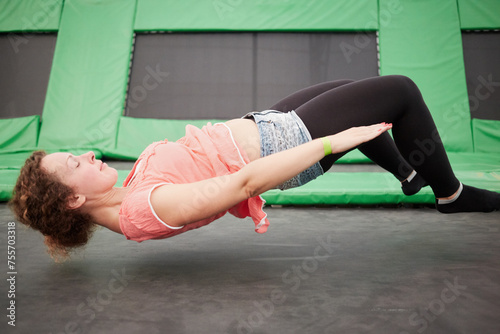 Young woman jumps on trampoline attraction in lying position