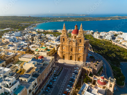 Aerial drone view of The Parish Church in Mellieha city and road. Blue sky, sea, day. Malta 