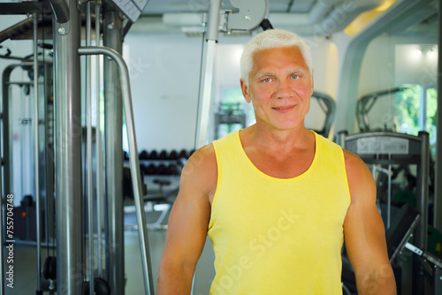 Middle-aged instructor stands in modern gym with fitness equipment