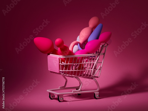 anal plugs and dildo sex toys in shopping basket over pink backdrop