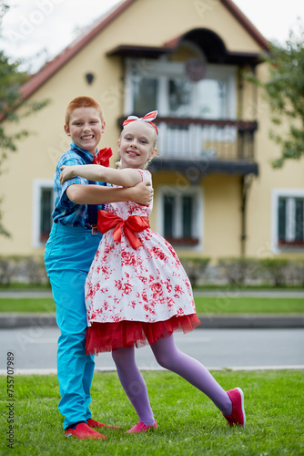 Boy and girl in dancing suits dance on grassy lawn against two-storied house photo