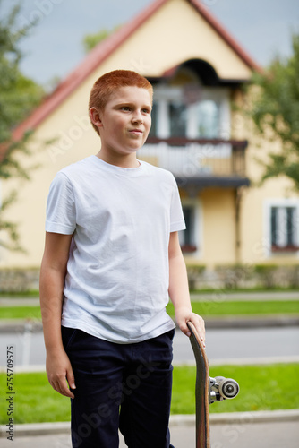 Portrait of red-haired boy with skateboard outdoor against house © Pavel Losevsky