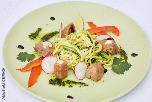 Plate of spaghetti with roasted meat and slices of radish, red pepper, lime and herbs