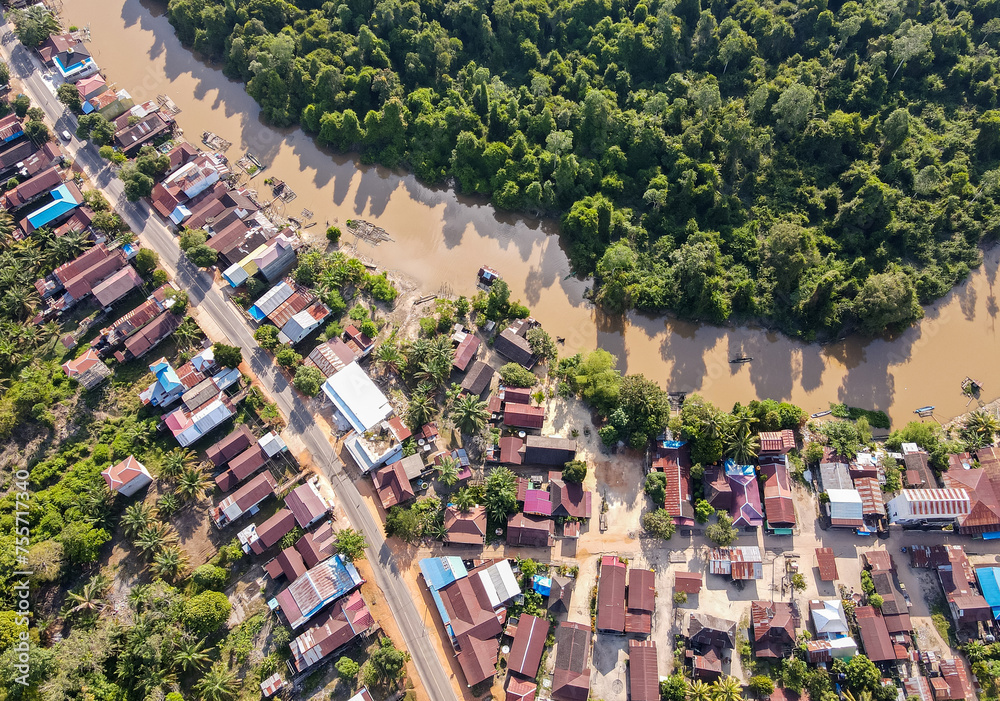 Residential center on the edge of a river and forest in a rural area, on the edge of a cross-regional road, in East Kotawaringin Regency, Central Kalimantan, Indonesia, seen from an aerial view. - obrazy, fototapety, plakaty 