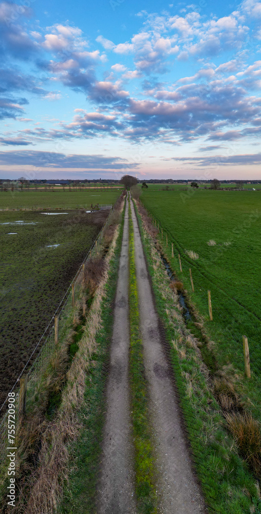 Ground-level shot captures the allure of a rural road vanishing into the distance under a sky painted with dusk's pastel hues. Country Road Embraced by Twilight Sky: Aerial Journey Through Farmland
