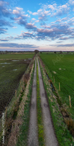 Ground-level shot captures the allure of a rural road vanishing into the distance under a sky painted with dusk's pastel hues. Country Road Embraced by Twilight Sky: Aerial Journey Through Farmland