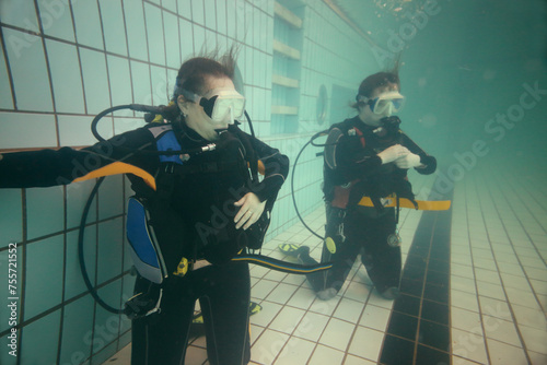 Two women are standing on knees with equipment for diving in the pool