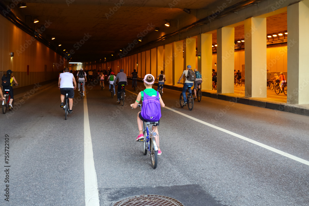 Many people ride bicycle in tunnel during bike parade in city, back view