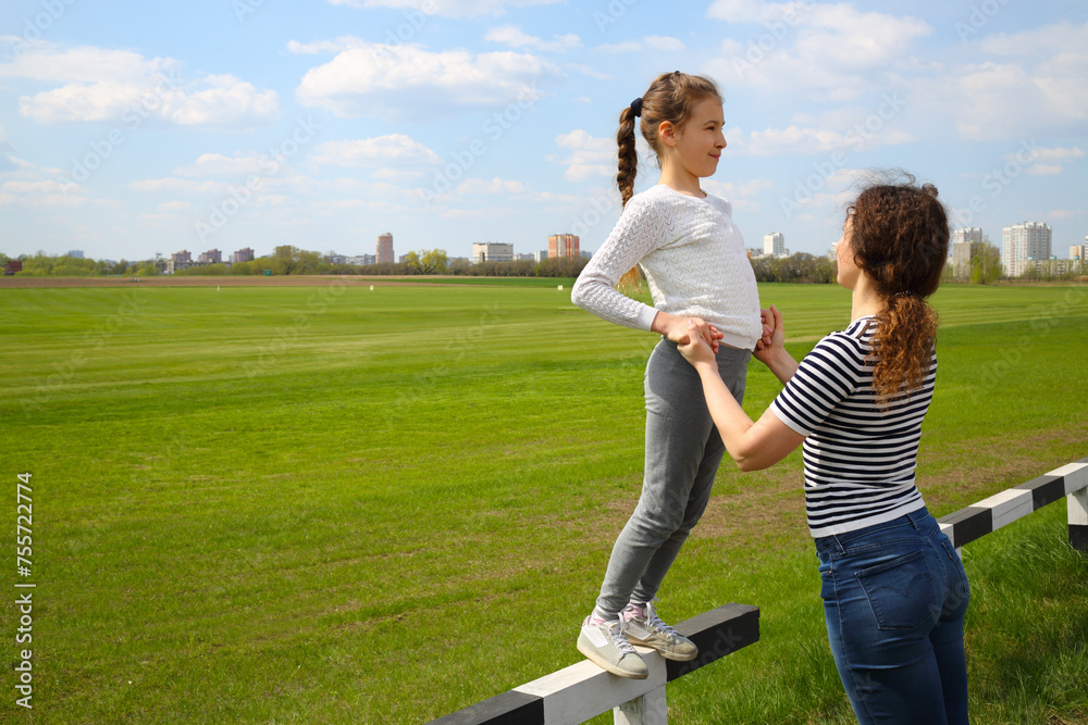 Happy pretty girl stands on fence with mother near green golf course Happy pretty girl stands on fence with mother near green golf course