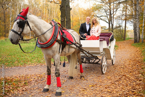 Man and woman are in coach with horse and hold reins in autumn park
