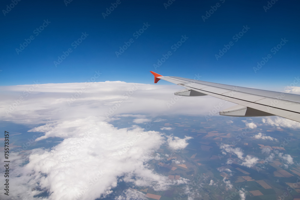 Fototapeta premium Wing of flying airplane, land, clouds in blue sky, view from window
