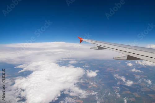 Wing of flying airplane, land, clouds in blue sky, view from window