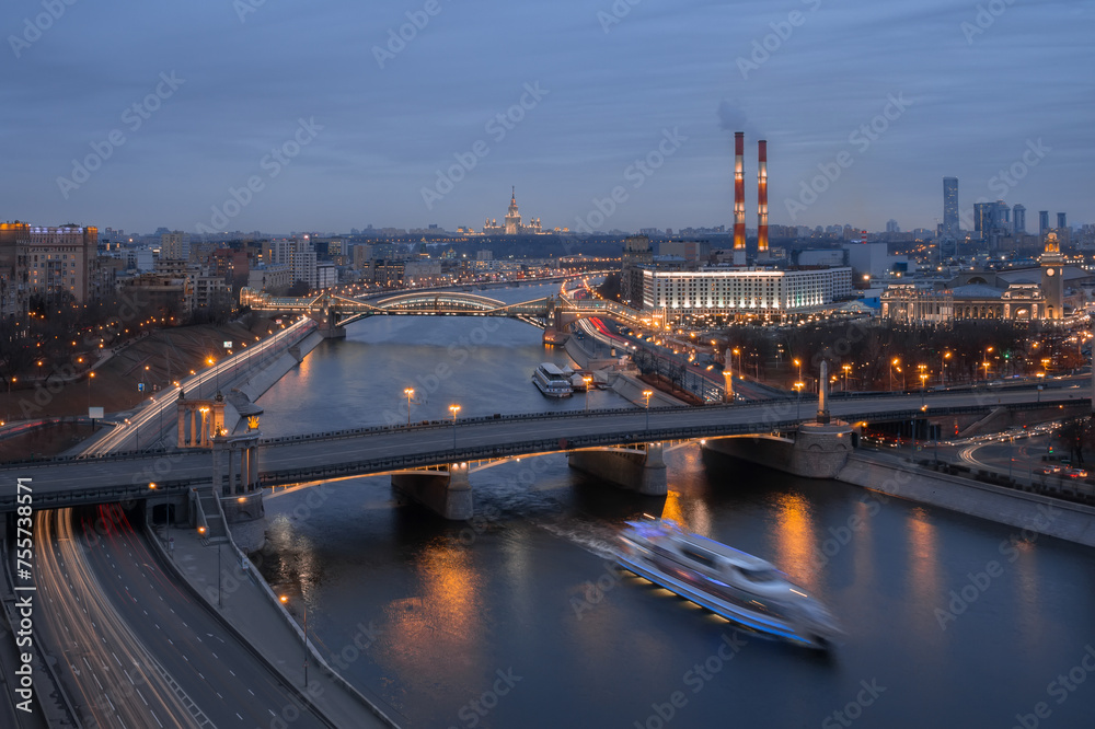 Borodinsky Bridge, river, factory pipes and panorama of city in Moscow, Russia at evening
