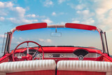 Driver view of a red vintage classic open American cabriolet car in front of a sunny blue sky