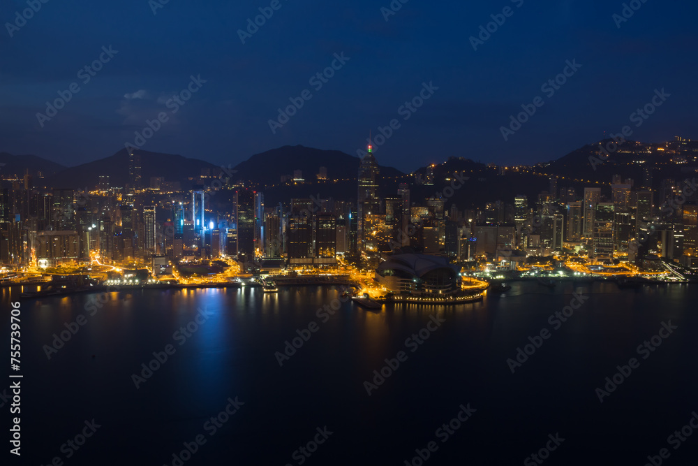 Skyscrapers with bright illumination, shore and mountains in Hong Kong, China at dark night, view from New World Center