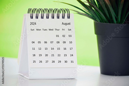 August 2024 desk calendar with potted plant on a desk with green background.