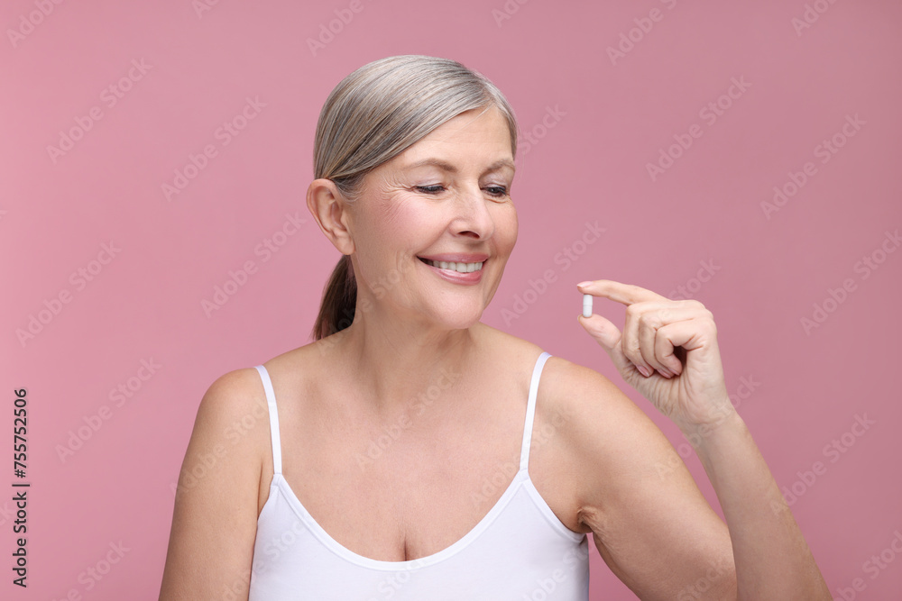 Beautiful woman with vitamin capsule on pink background