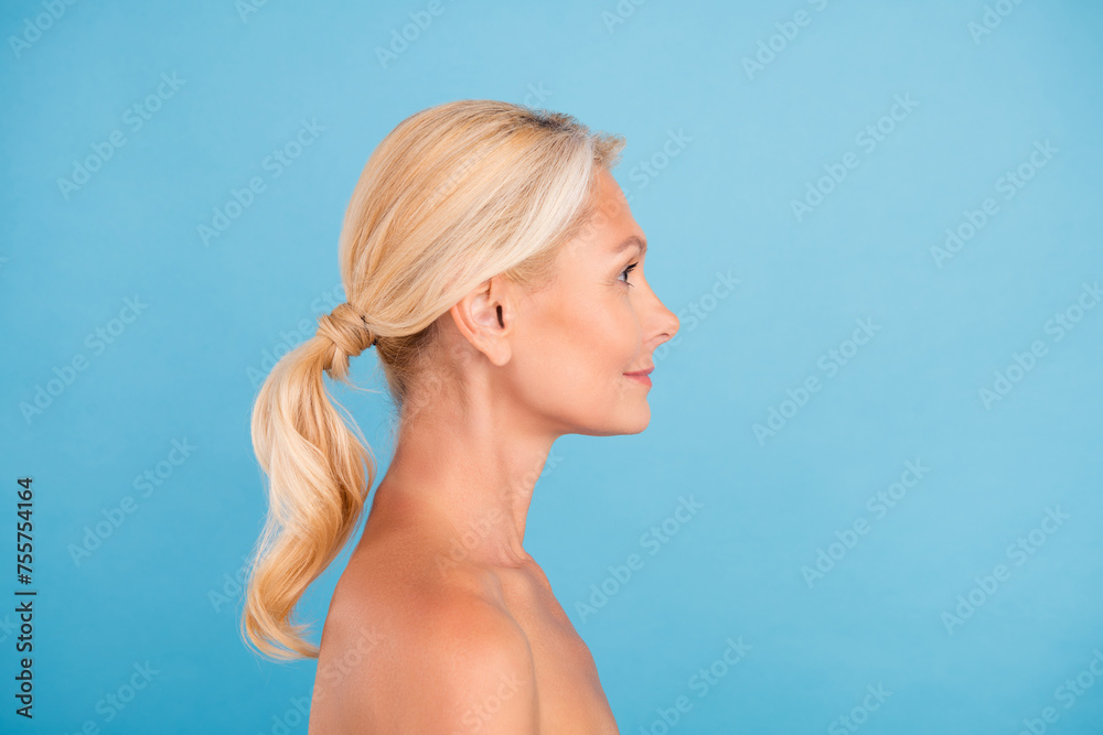 Profile side photo of pretty adorable elderly lady naked shoulders smiling looking empty space isolated blue color background Profile side photo of pretty adorable elderly lady naked shoulders smiling looking empty space isolated blue color background