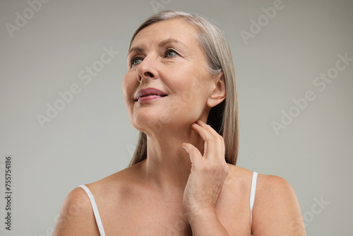 Beautiful woman touching her neck on grey background, low angle view