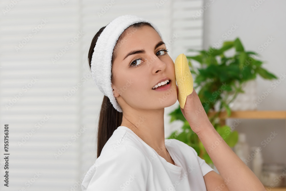 Young woman with headband washing her face using sponge in bathroom Young woman with headband washing her face using sponge in bathroom