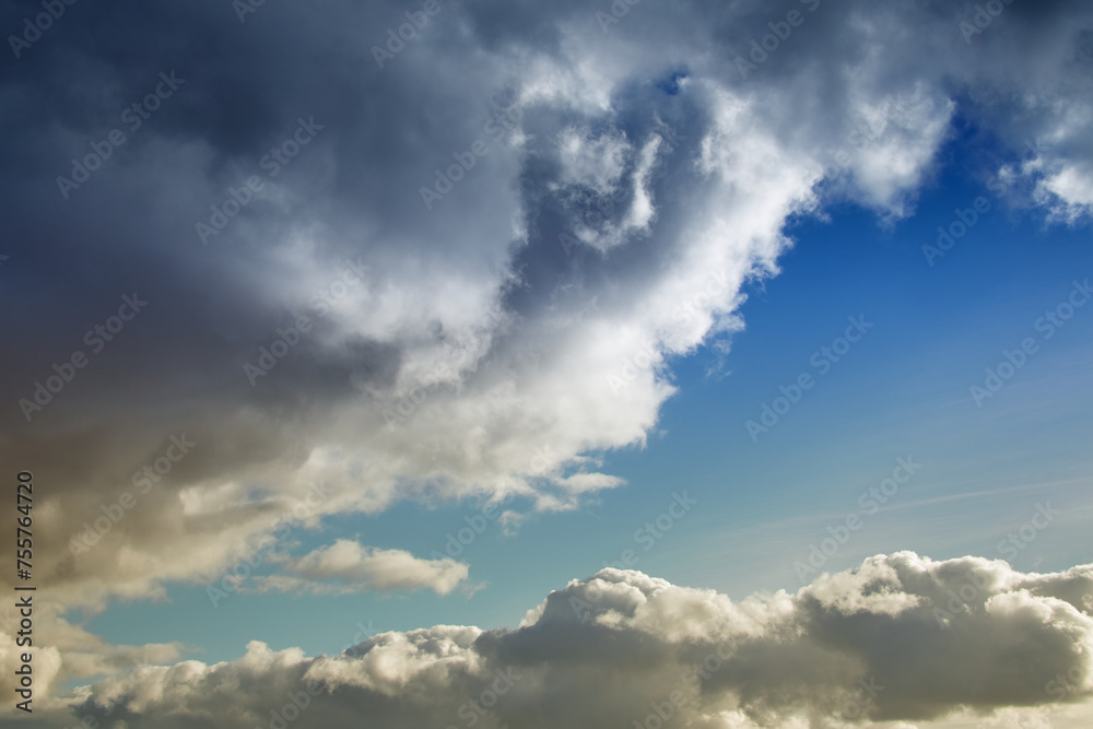 Large cumulonimbus rain clouds cover the blue sky, a cloud in warm sunlight on the blue sky