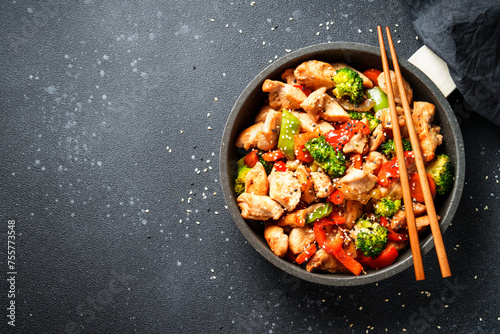 Stir fry chicken and vegetables and sesame at black background. Asian cuisine. Top view with space for design.