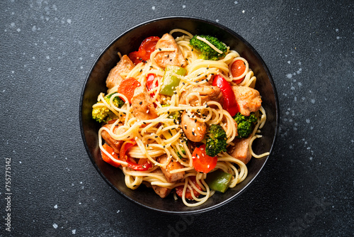 Stir fry chicken with vegetables and noodles at black background. Asian cuisine. Top view with space for design. © nadianb