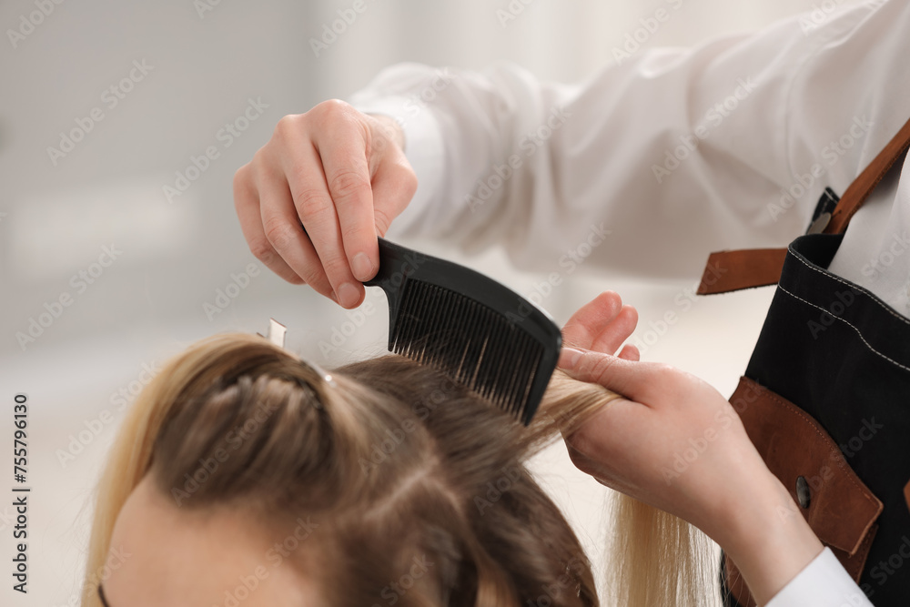 Naklejka premium Hair styling. Professional hairdresser combing woman's hair in salon, closeup