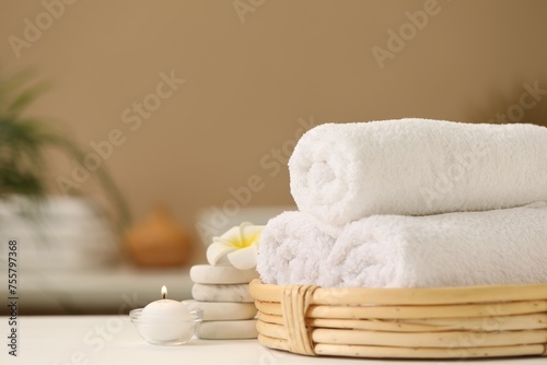 Spa composition. Rolled towels, massage stones, burning candle and plumeria flower on table. Space for text